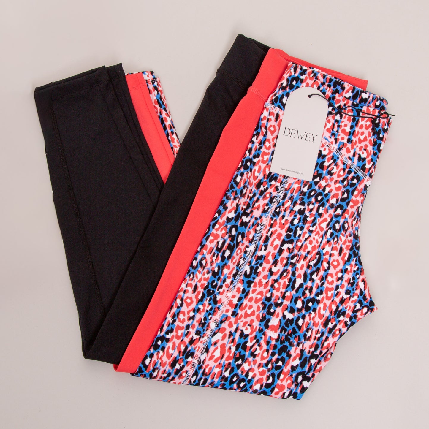 Three pairs of DEWEY IRIS High Waist Leggings (Printed, Extra Petite) in black, bright coral, and blue-red leopard print are displayed on a plain light background. The patterned pair has a white DEWEY tag—ideal for athleisure.