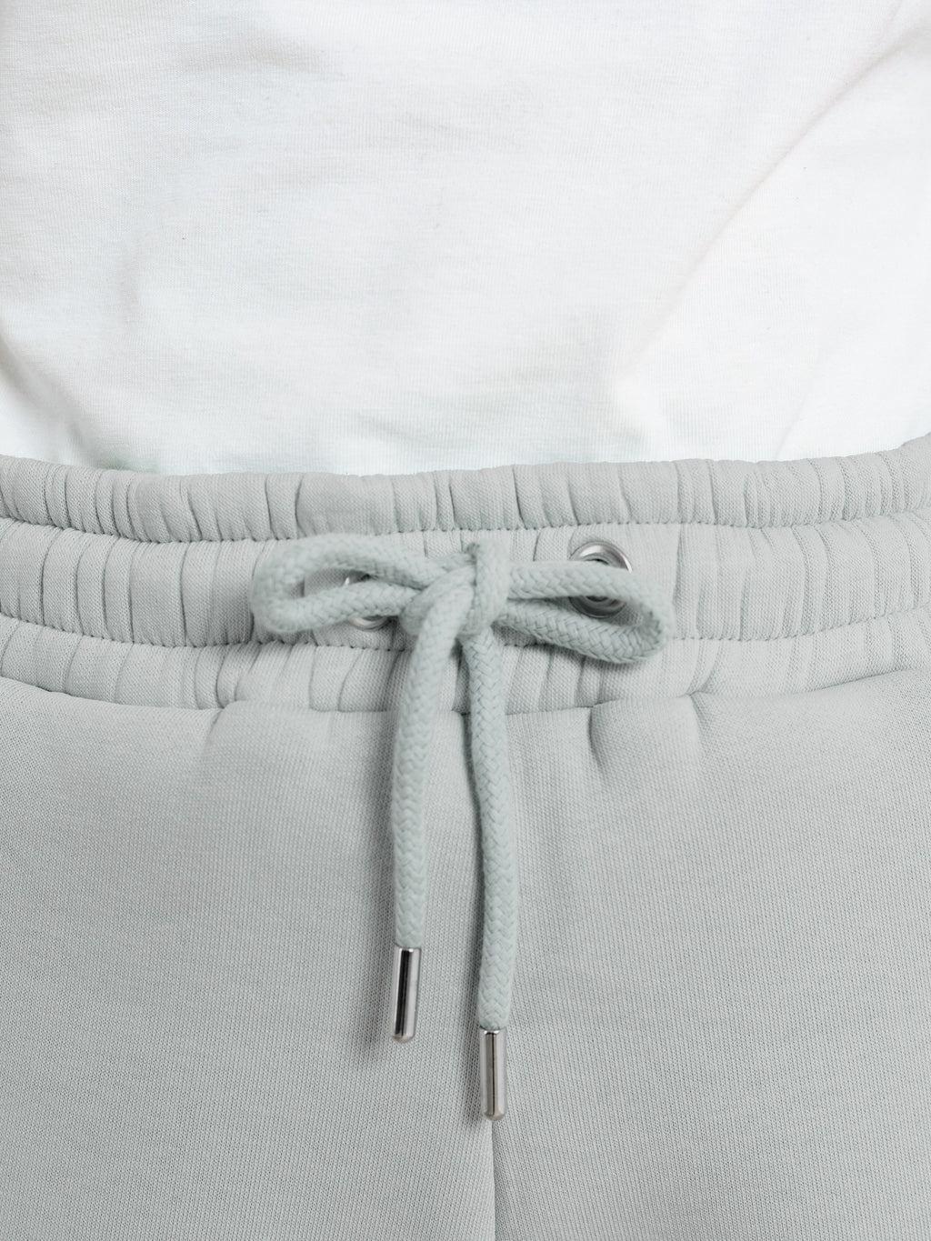 Close-up of elevated loungewear: a person wears DEWEY's RILEY Sweat Shorts in grey (Extra Petite) with a drawstring tied in a bow, paired with a white shirt tucked at the waist.